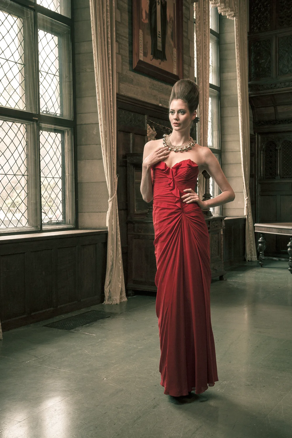 Fashion portrait of a woman wearing a red gown beside tall leaded windows